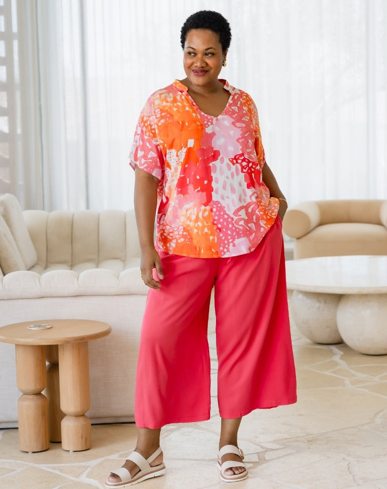 Woman wearing a colorful top and pink pants in a living room setting